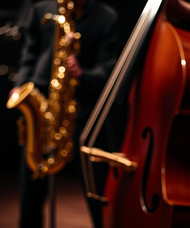 Primer plano de un saxofón y un contrabajo en un escenario con poca luz.